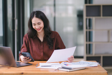 Asian businesswoman or accountant using a calculator, graphs, and charts to analyze market data, balance sheets, accounts, and net profits.