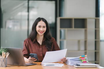 Asian businesswoman or accountant using a calculator, graphs, and charts to analyze market data, balance sheets, accounts, and net profits.