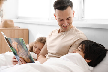 Father reading story to his little children in bedroom