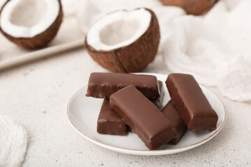 Plate with tasty chocolate covered coconut candies on light background