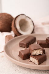 Plate with tasty chocolate covered coconut candies on light background