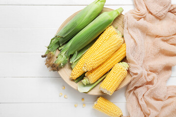 Plate with fresh corn cobs on white wooden table