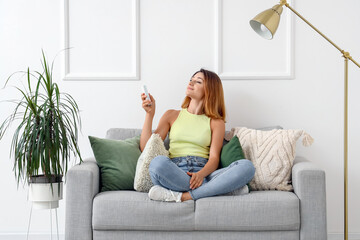 Obraz premium Young woman switching on air conditioner at home