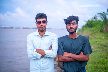 Portrait of south asian young boys with sunglasses on their eyes standing in front of a river 