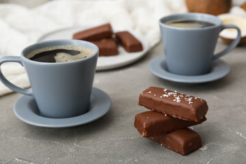 Tasty chocolate covered coconut candies and cups of coffee on grey background
