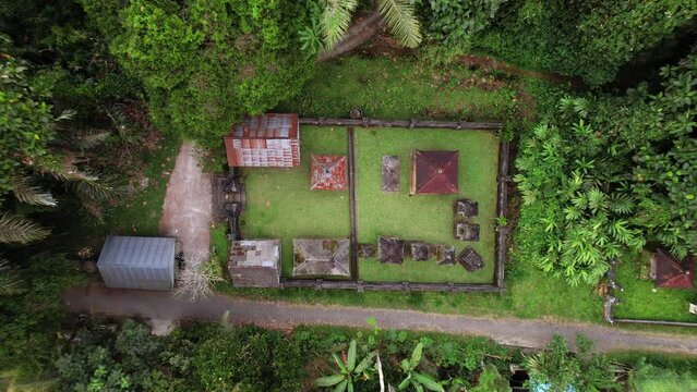 Top-down view of small Hindu temple at outskirts of Balinese village, camera fly up and reveal surroundings. Lush tropical forest seen at one side, rice plantations at other side
