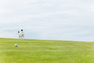 青空の見える公園を走る兄弟の後ろ姿・少年とサッカーボール  © buritora