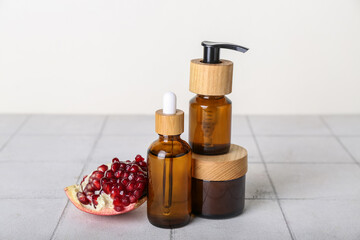 Set of cosmetic products and pomegranate on tile table against light background