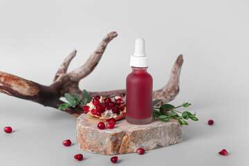 Composition with bottle of essential oil, pomegranate and tree branch on light background