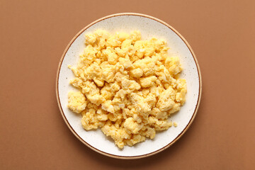 Plate of tasty scrambled eggs on brown background