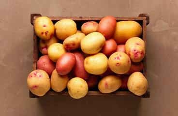 Wooden box with fresh raw potatoes on brown background