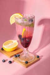 Glass of fresh blueberry lemonade on pink background