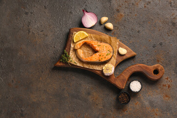 Wooden board of tasty salmon steak with garlic, onion and lemon on brown background