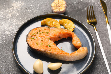 Plate of tasty salmon steak with lemon and garlic on grey background