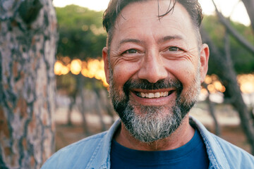 Close up portrait looking on camera of adult mature man with beard and big smile at the park. Aged...
