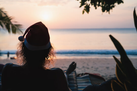 Man with backlit hair and santa hat enjoying the view of the tropical sunset at the beach, Thailand - Powered by Adobe