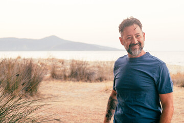 Cheerful man walking outdoor happy looking on camera. Scenic travel destination background with beach and ocean island. Clear white sky copy space. Casual clothes blue T-Shirt. Journey lifestyle