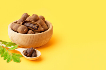 Bowl and spoon of tasty tamarinds on yellow background
