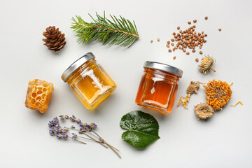 Jars with tasty honey, honeycomb, dried flowers and raw buckwheat on white background