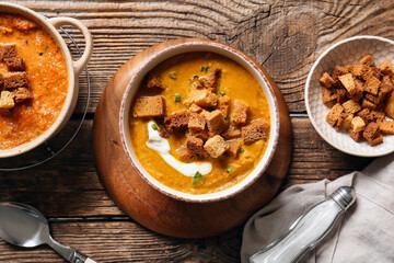 Pot and bowl of tasty cream soup with croutons on wooden background