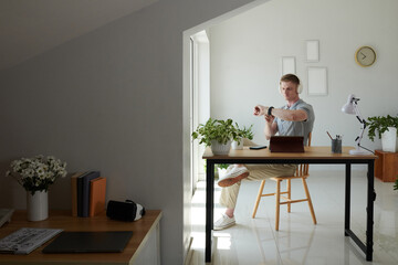 Freelancer in headlines sitting at desk in home office and checking notification on smartwatch
