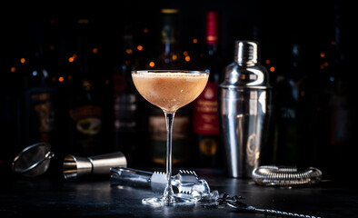 Rattlesnake coffee cocktail drink with cocoa liquor, irish cream, ground coffee and ice in glass, dark bar counter background, bar tools and bottles