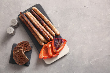 Board of tasty grilled sausages, bread and vegetables on grey background