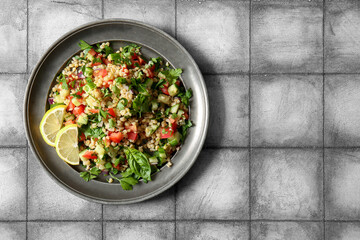 Plate with delicious tabbouleh salad and lemon slices on tile grey background