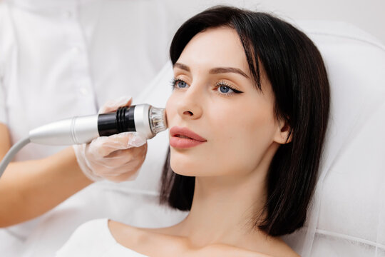 Attractive young woman undergoing a cosmetic procedure in a beauty salon. A woman undergoes fractional RF lifting against a light background. Advertising concept for clean and young facial skin.