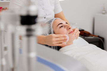 A cosmetologist cleanses the facial skin with napkins before a professional cosmetic procedure in a beauty salon for a client. Skin care and cosmetology spa concept.