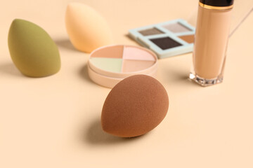 Makeup sponges with decorative cosmetics on color background