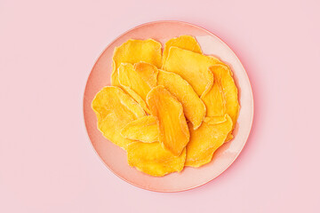 Plate with slices of dried mango on pink background