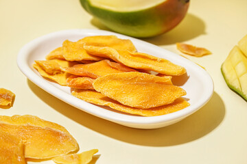 Plate with slices of dried mango on yellow background