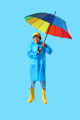 African-American little boy in raincoat with umbrella jumping on blue background