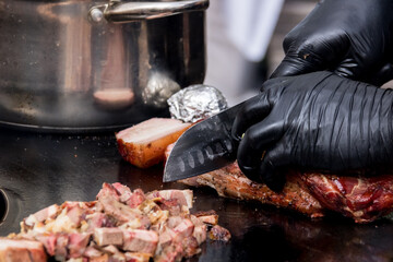 A man's hand cuts fried meat with a butcher knife on a cutting board made of slate. Rustic style