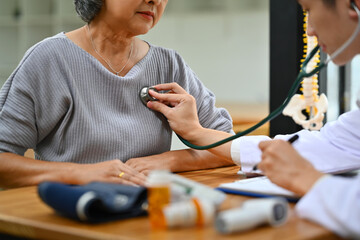 Male healthcare worker using stethoscope checking heart and lungs of senior woman. Elderly healthcare concept