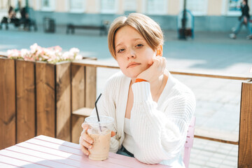 A teenage girl sits at a table in a cafe with a cold drink in a glass. 