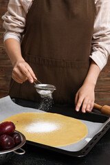 Woman preparing delicious plum galette on black table