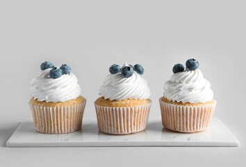 Board of tasty cupcakes with blueberries on grey background
