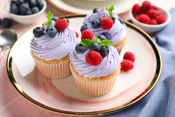 Plate of delicious cupcakes with blueberries, raspberries and mint on pink tile background