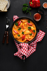 Chicken paprikash dish with paprika, onion, sweet pepper in black pan with red napkin on dark...