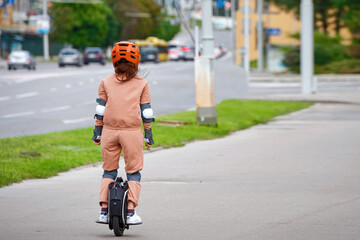 Woman in protective gear riding electric unicycle, monocycle or mono wheel. Trendy woman in helmet on electric vehicle, view from back. Woman ride electric mono wheel, personal electric transport © Tricky Shark