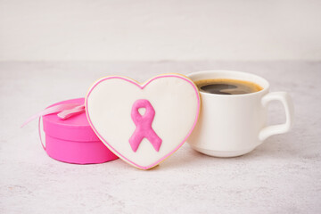 Cookie in shape of heart with pink ribbon and cup of coffee on white grunge background. Breast cancer awareness concept