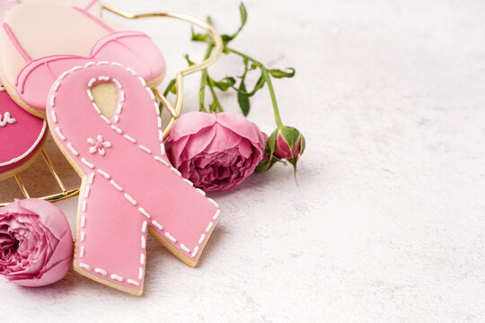 Pink cookie in shape of ribbon and rose flowers on white grunge background. Breast cancer awareness concept