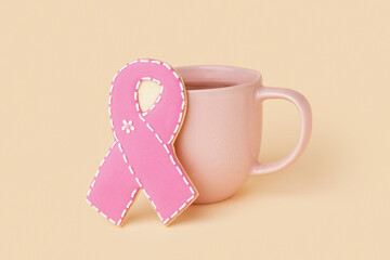 Pink cookie in shape of ribbon and cup of coffee on beige background. Breast cancer awareness...