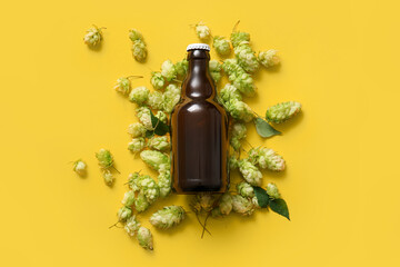 Fresh green hops and bottle of cold beer on yellow background