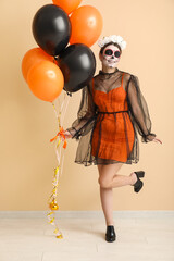 Young woman dressed for Halloween with balloons near beige wall