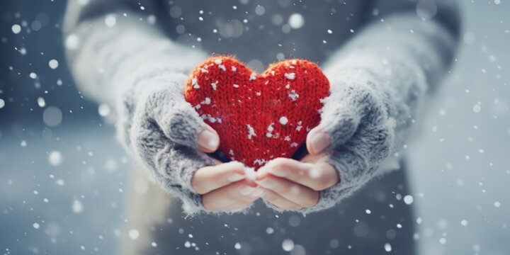 Female hands in knitted mittens with knitted heart on a snowy winter day