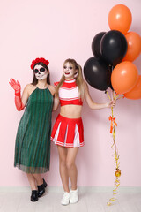 Female friends dressed for Halloween with balloons near pink wall