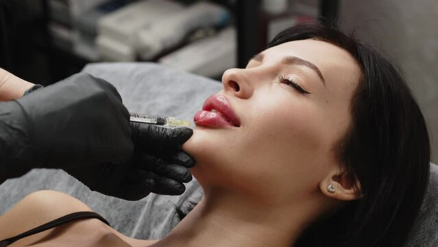 Injection procedure for lip augmentation, close-up. The cosmetologist slowly and carefully injects filler into the client&rsquo;s lips. Advertising concept for facial care, youth and beauty.